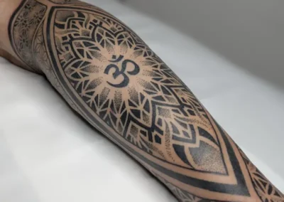 Tatouage ornemental et géométrique noir sur le mollet , avec motif mandala et indien, lignes symétriques et dotwork