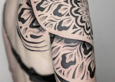 Tatouage ornemental et géométrique noir sur l'épaule. Motif mandala, lignes symétriques et dotwork