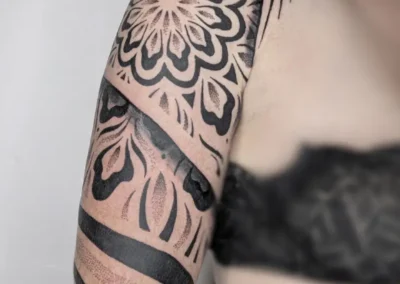 Tatouage ornemental et géométrique noir sur l'épaule et le bras, motif mandala, lignes symétriques et dotwork